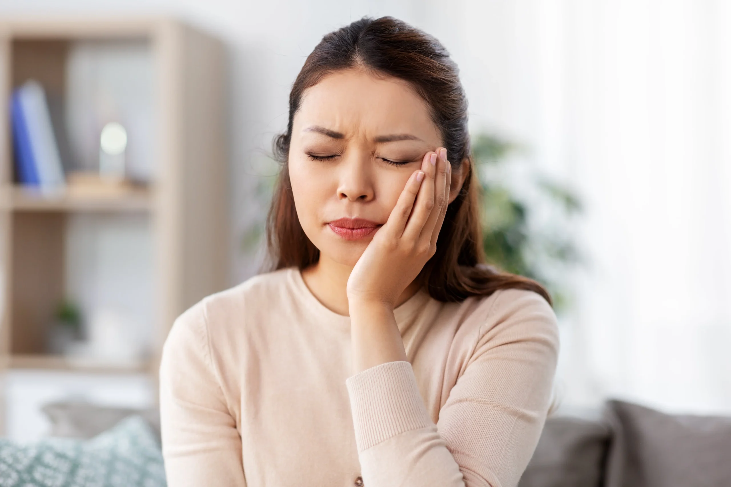 Young Woman seated on a couch holding her hand to her face in pain