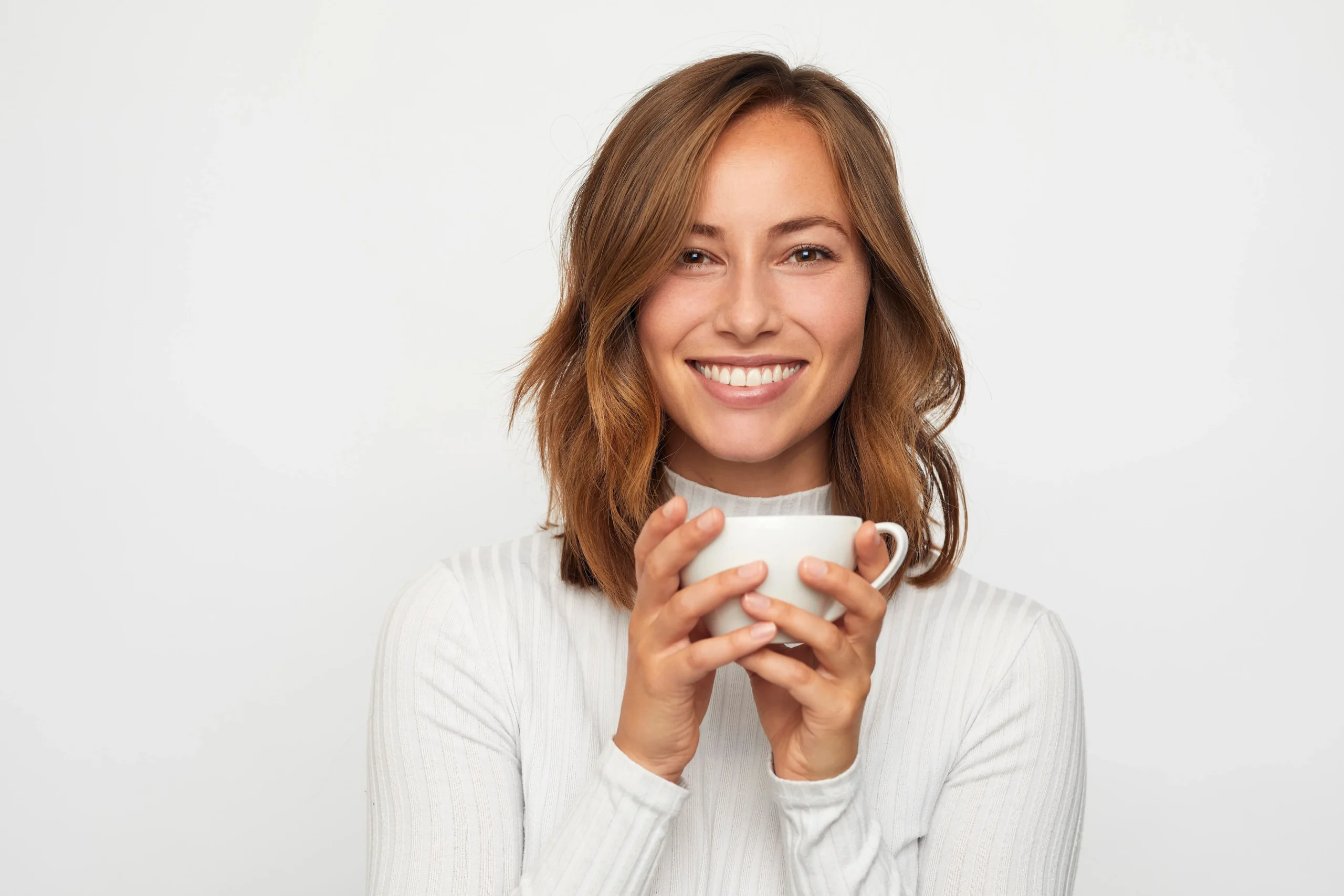 A woman holding a coffee cup in her hands while smiling